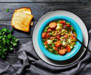 Smoked sausage soup in a bowl on a table with toast fresh herbs and table cloth.